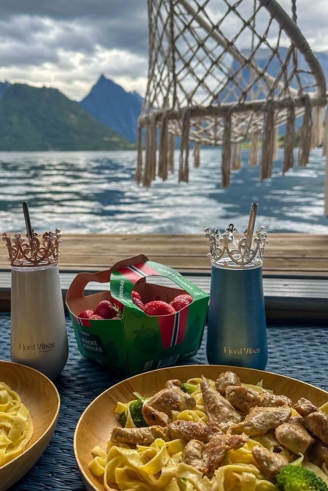 to middagstallerkener i vinduet mot en fjord, med prosecco kopper fra Fjord Vibes i hhv blå og hvit med hver sin pyntekrone og sugerør