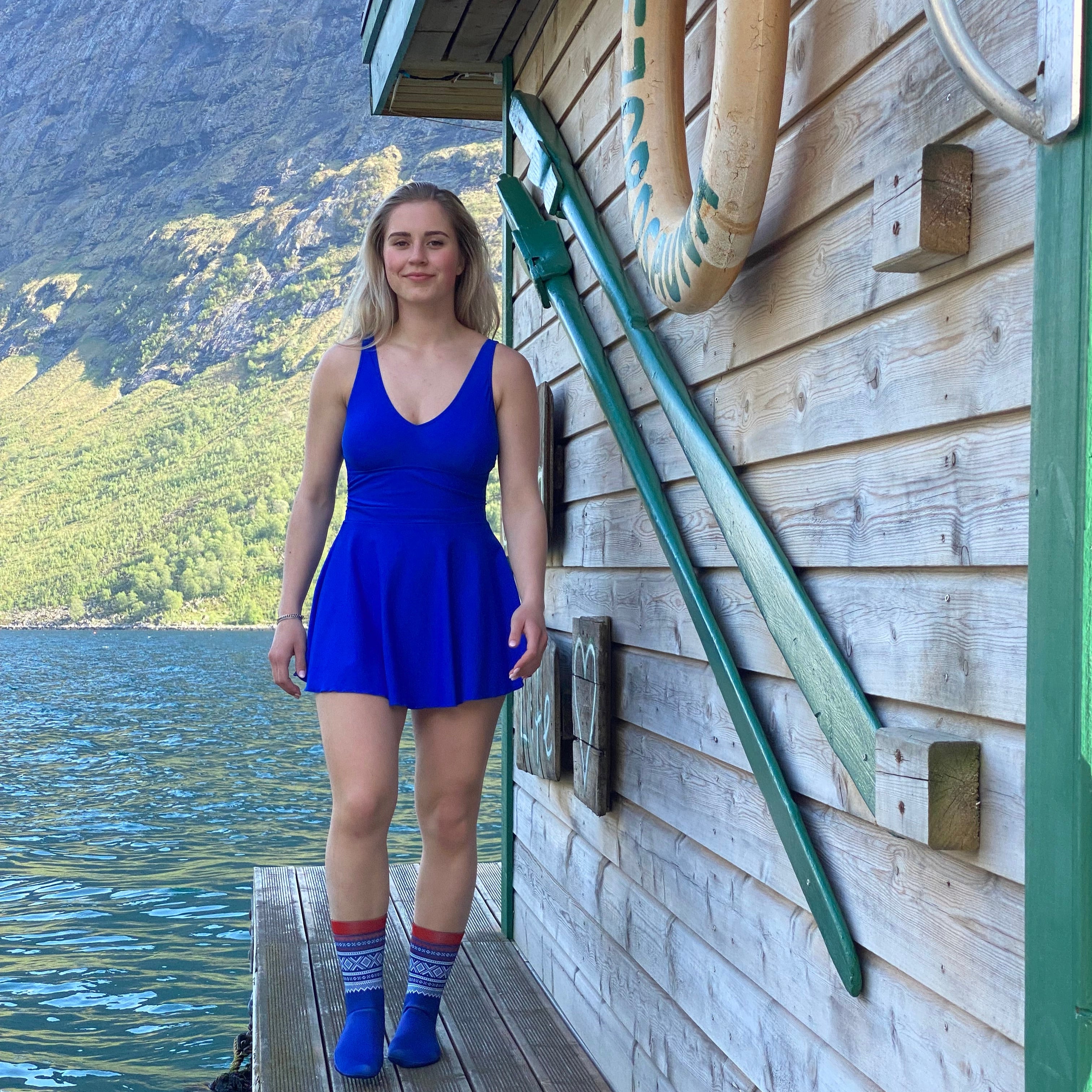 Dame som går på en brygge utenfor en sauna og har på en blå badekjole og blå Marius Neopren sokker